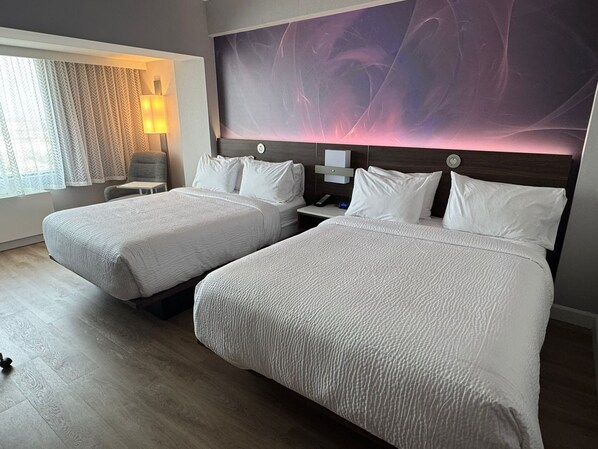 Habitación de hotel con dos camas, una mesita de noche, una lámpara y un cuadro abstracto grande en la pared.