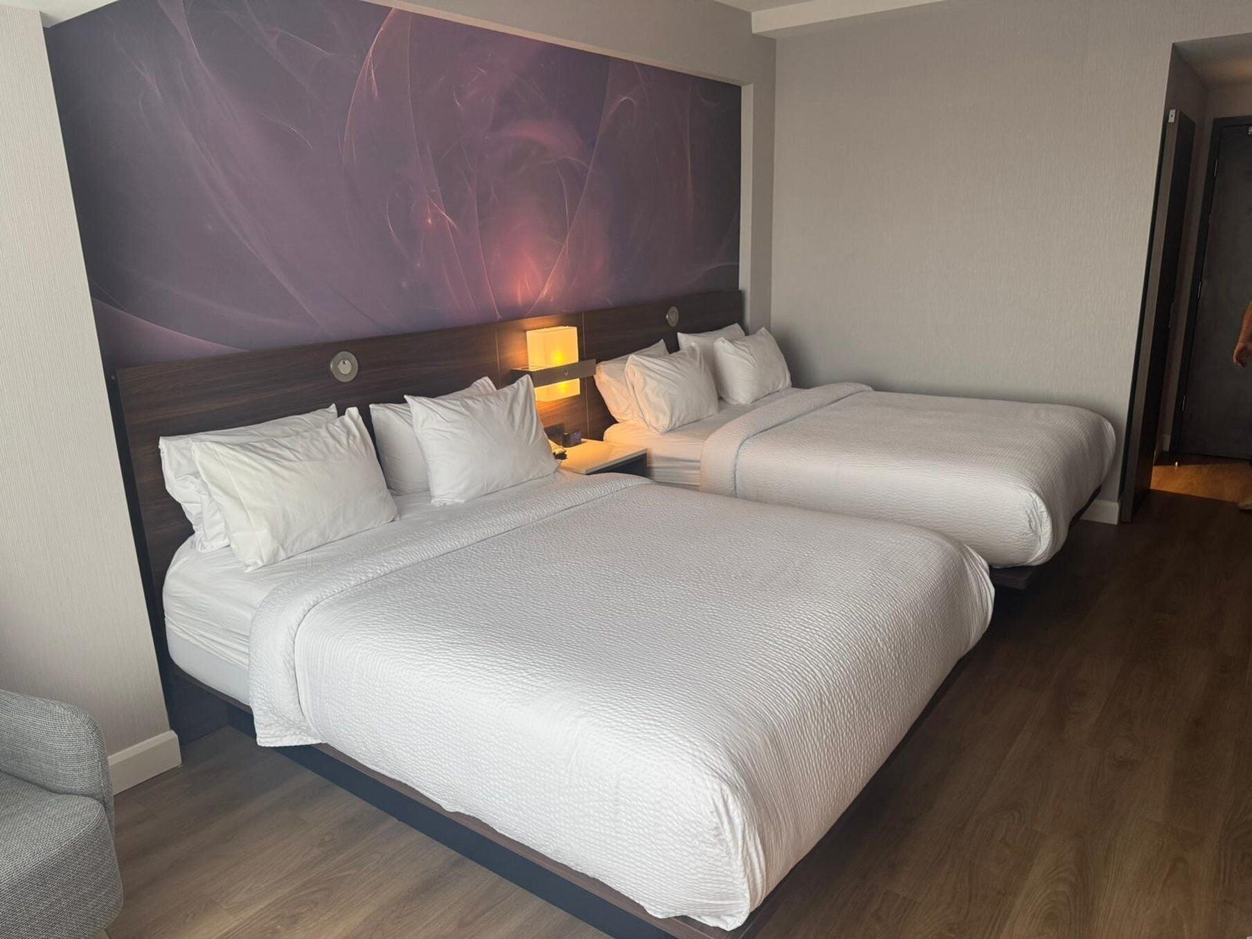 Una cama doble con sábanas blancas, una mesita de noche con lámpara y un cuadro abstracto grande en la pared.