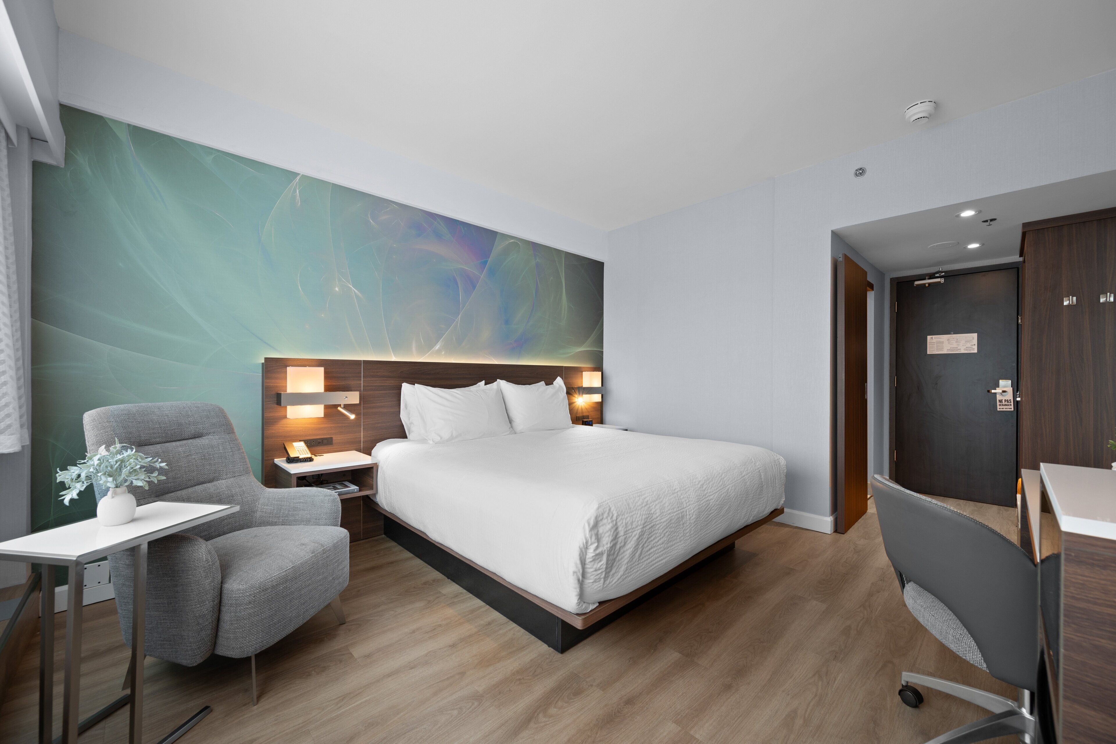 Ein modernes Hotelzimmer mit einem großen Bett, einem Schreibtisch, einem Stuhl und einem Nachttisch.