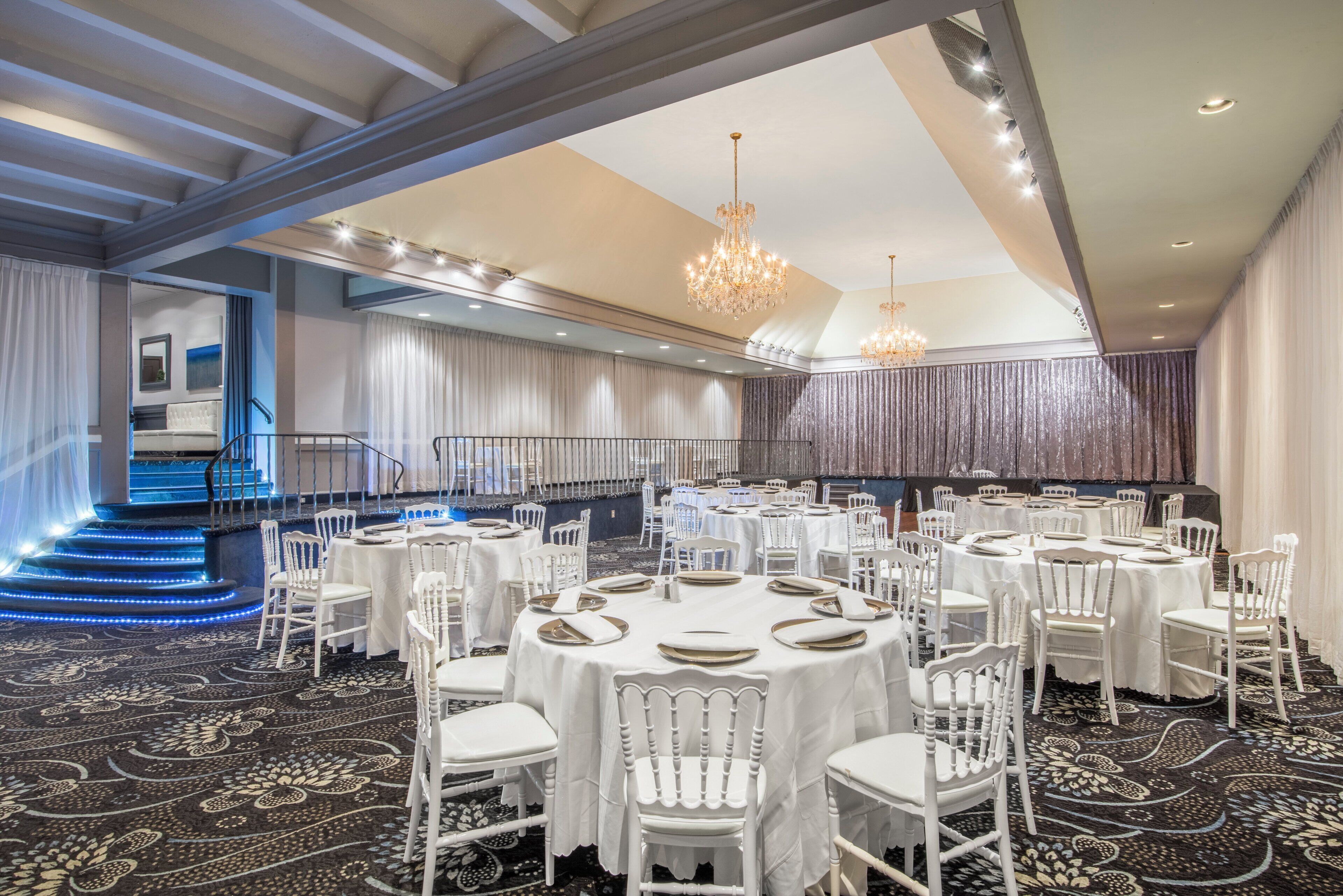 A banquet hall with round tables, white chairs, and chandeliers.