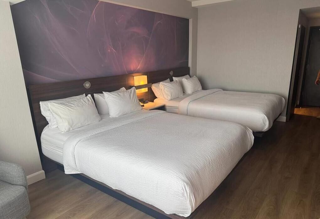 A hotel room with two beds, a large abstract mural on the wall, and a wooden floor.