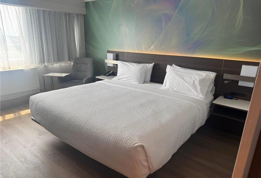 A hotel room with a large bed, a desk, a chair, and a wall-mounted TV.
