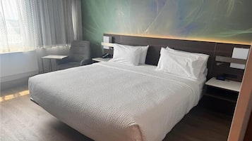 Une chambre d’hôtel avec un grand lit, un bureau, une chaise et un téléviseur fixé au mur.