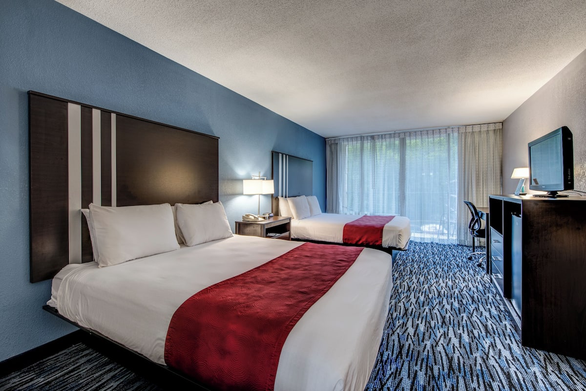 A hotel room with two beds, a desk, a TV, and a window with curtains.