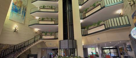 Un atrio de varios niveles con una escalera central, balcones con plantas y zonas de descanso.