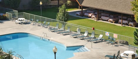 Piscina con sillas y mesas de descanso, un área de estar techada y un patio cercado.