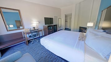 A hotel room with a large bed, a desk with a computer, a TV, and a mirror.
