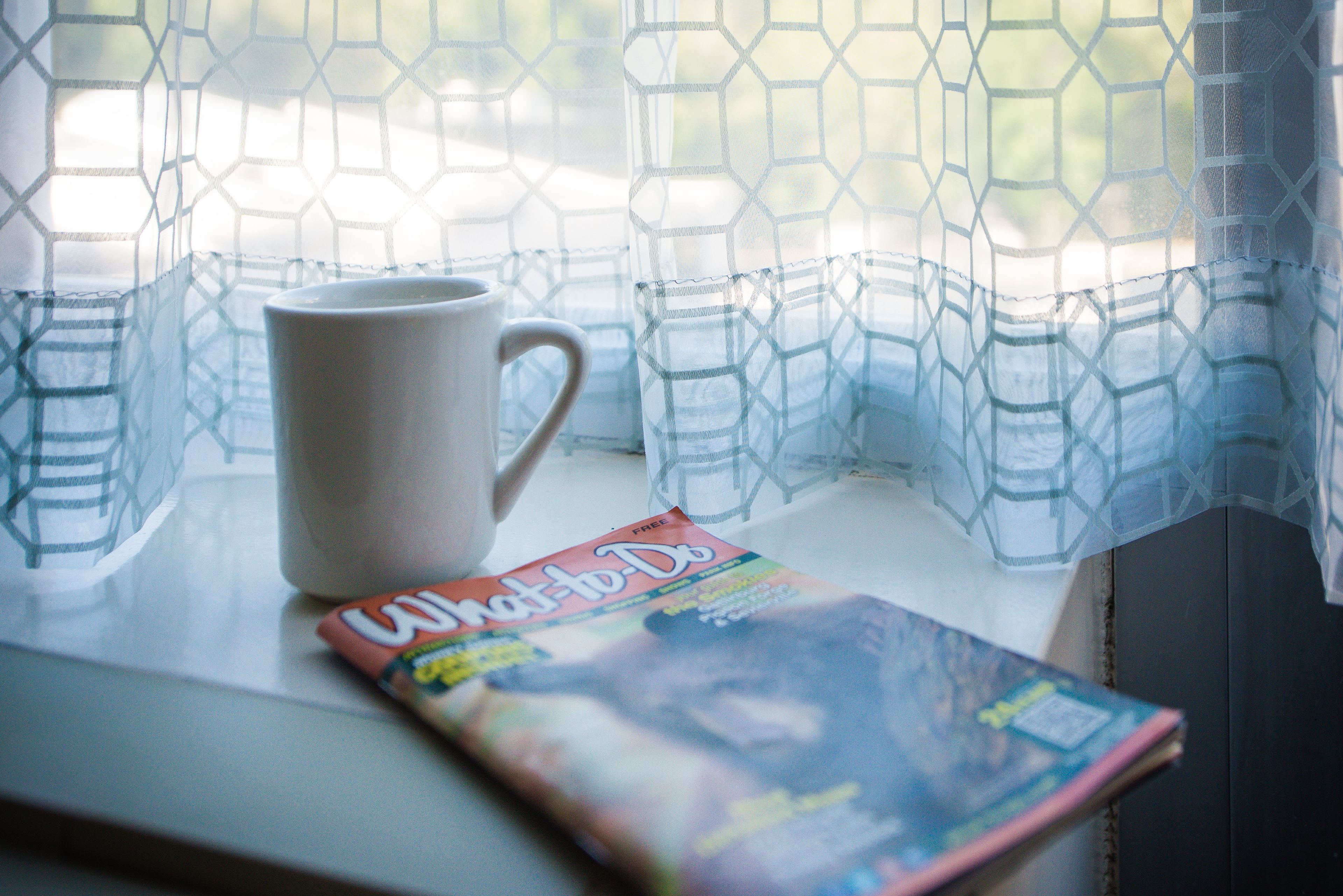 Eine weiße Tasse und eine Zeitschrift auf einem Fensterbrett.