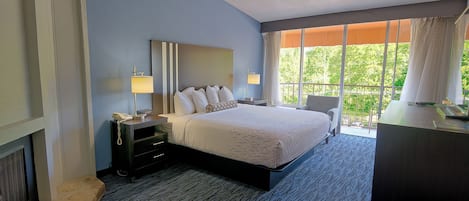 A hotel room with a large bed, bedside lamps, a desk, and a view of greenery through the window.