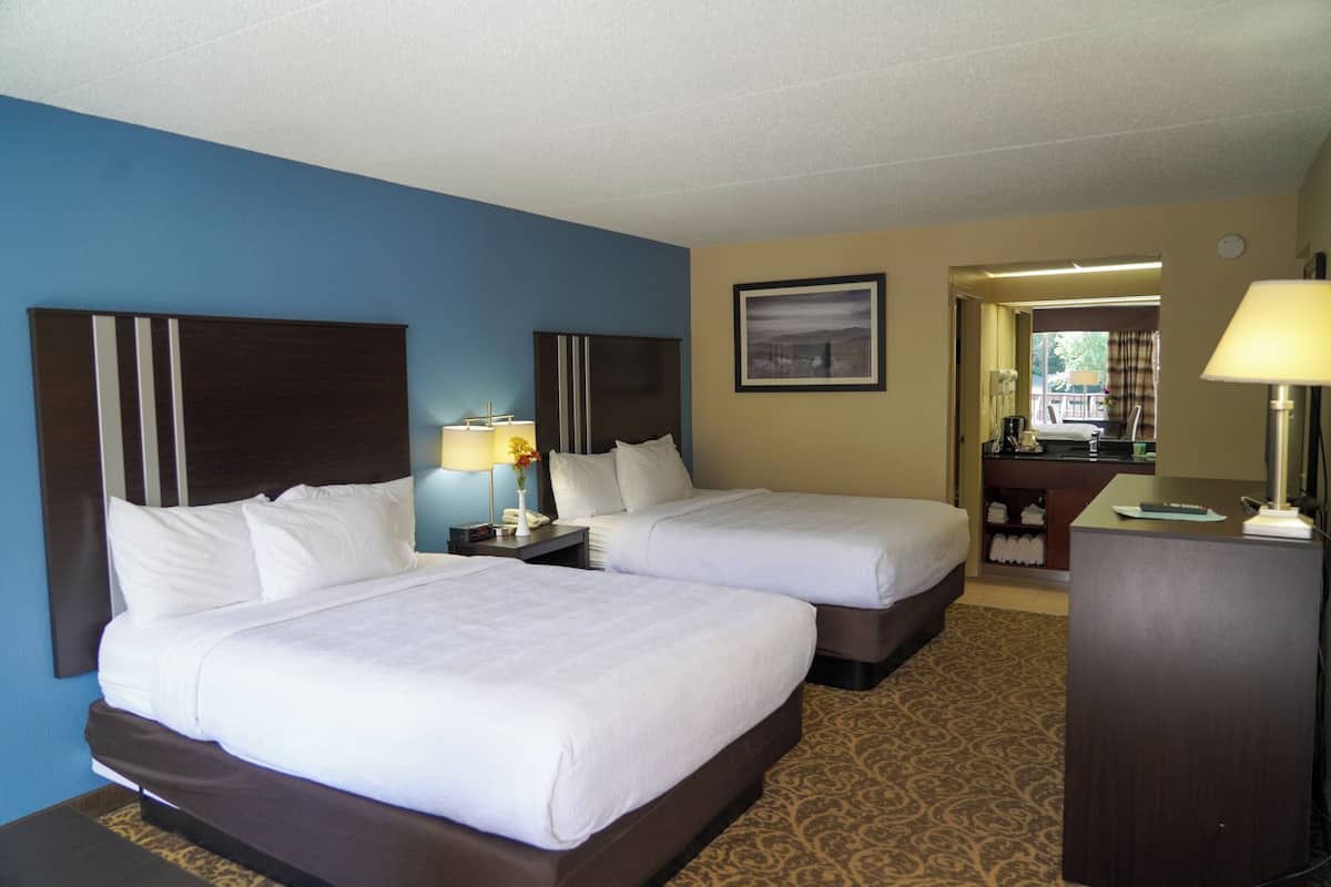 A hotel room with two beds, a desk, a lamp, and a painting on the wall.