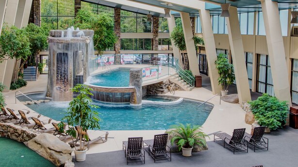 An indoor pool with a waterfall feature, surrounded by lounge chairs and potted plants.