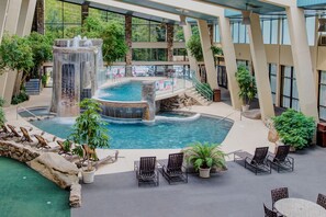 Una piscina interior con una cascada, rodeada de sillones de descanso y plantas en macetas.