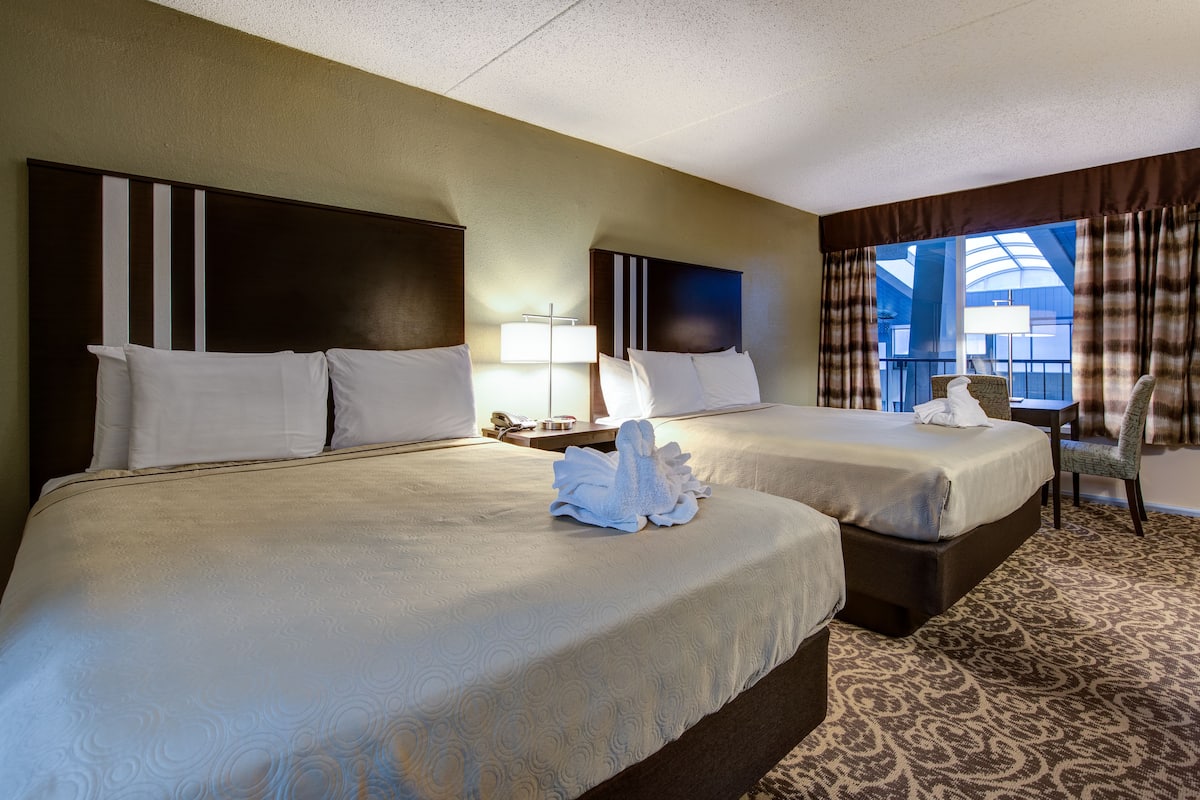 A hotel room with two beds, a large window with curtains, a chair, and a lamp.