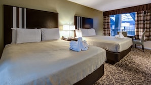 A hotel room with two beds, a large window with curtains, a chair, and a lamp.