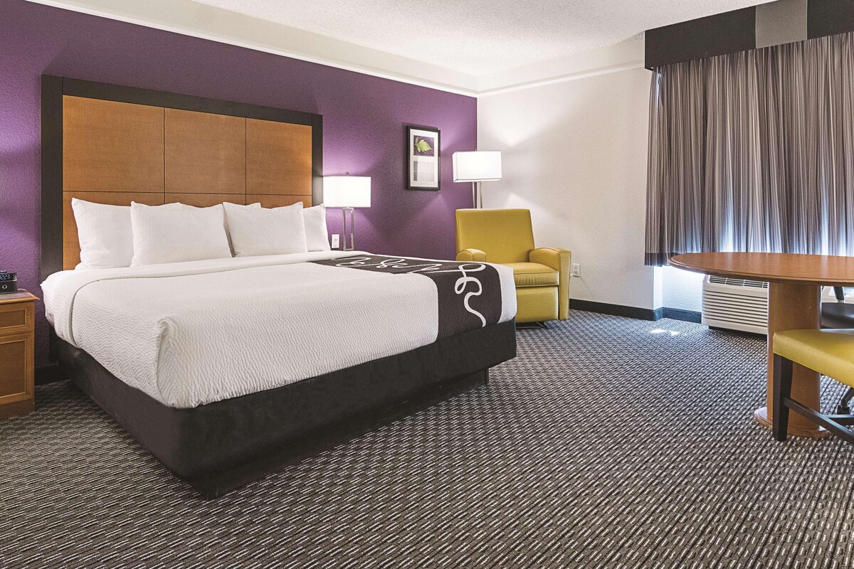 A hotel room with a large bed, a chair, a table, and a lamp.