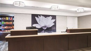 A reception desk with a large floral artwork, a snack shelf, and a white door in the background. - La Quinta Inn by Wyndham Denver Westminster (Westminster)