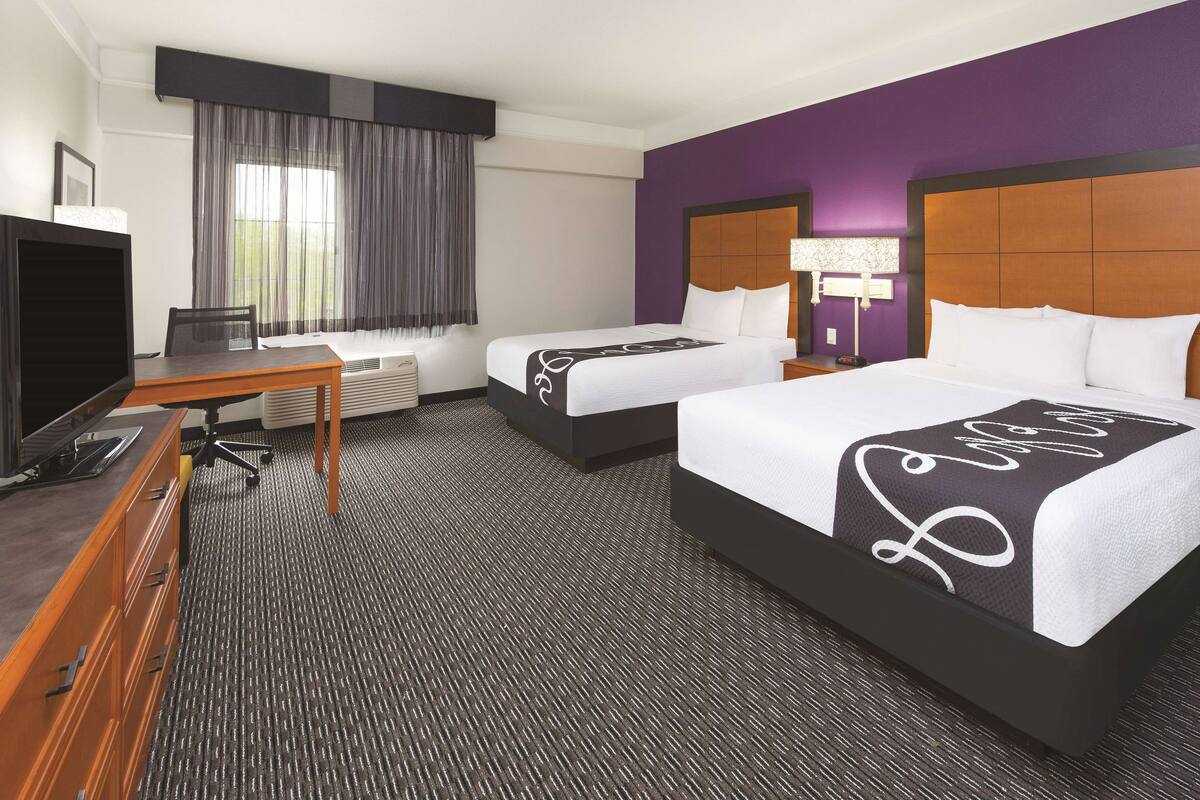 A hotel room with two beds, a desk with a computer, a television, and a window with curtains.