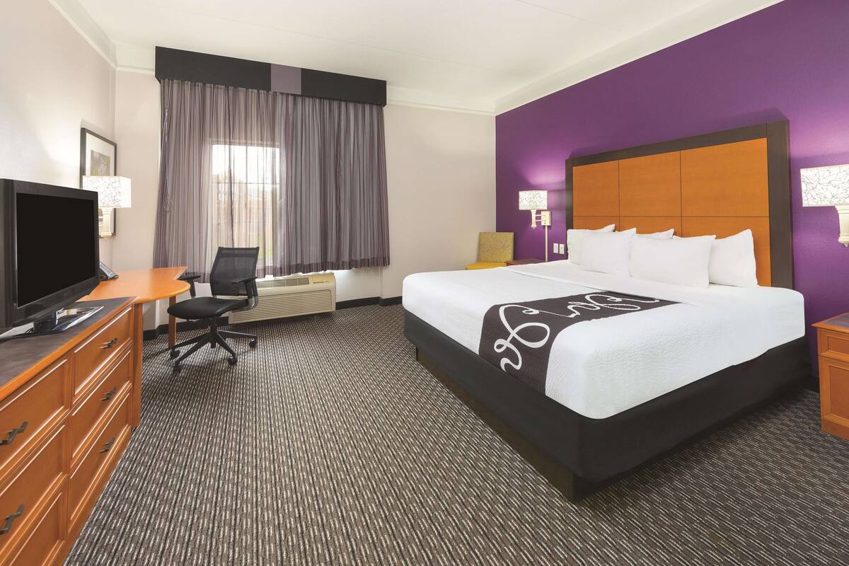 A hotel room with a large bed, a desk with a chair, a television, and a window with curtains.