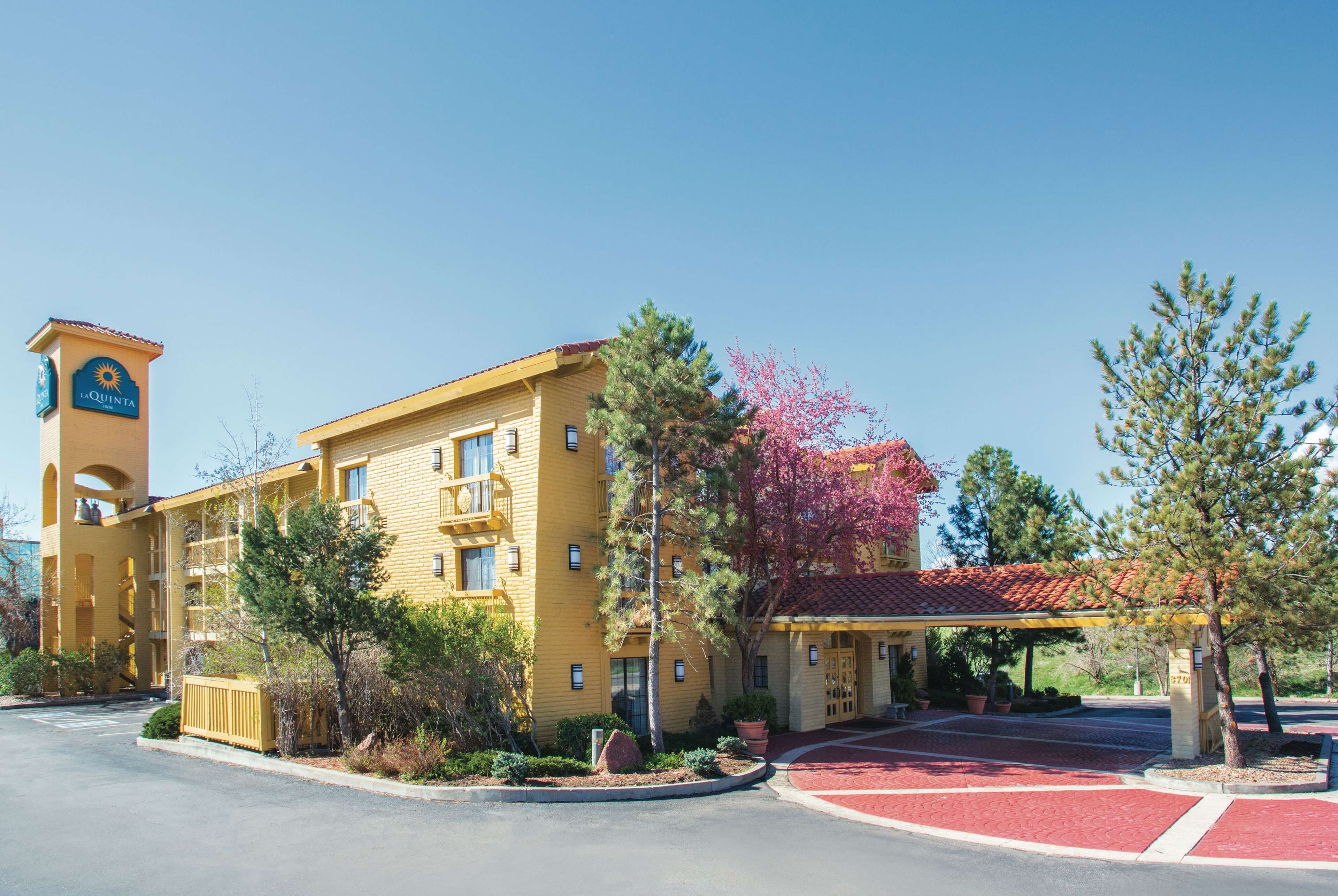 Un hotel amarillo con una torre, un estacionamiento techado y un camino rojo.