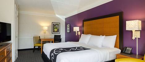 A hotel room with a large bed, a desk, a chair, a television, and a telephone.