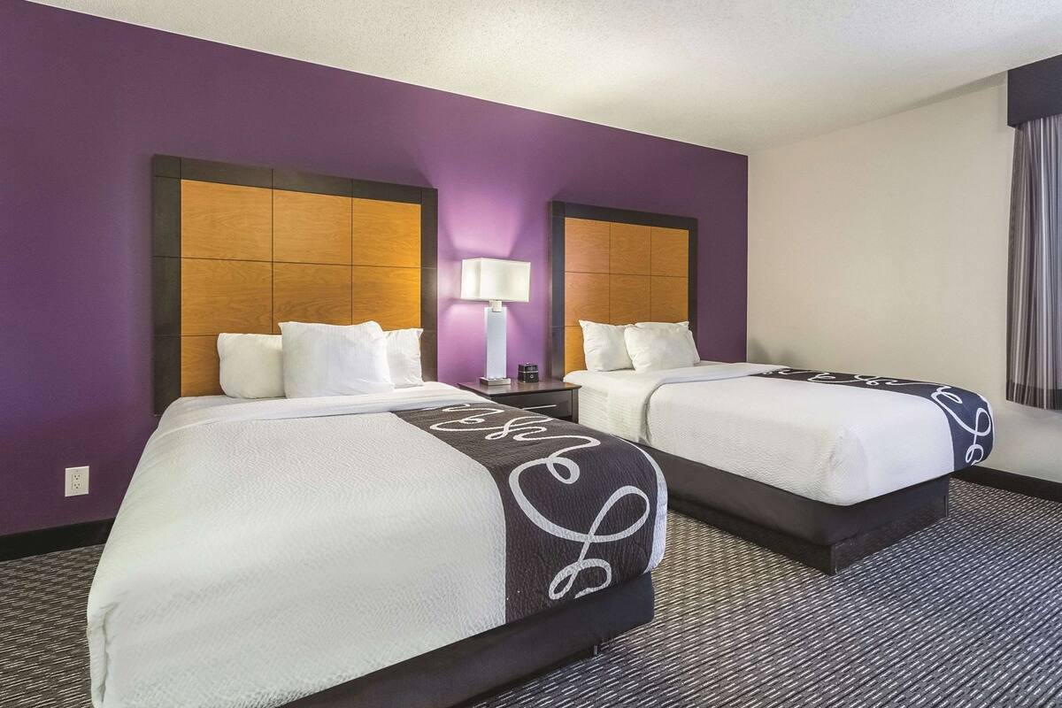 A hotel room with two beds, a nightstand with a lamp, and a window with curtains.