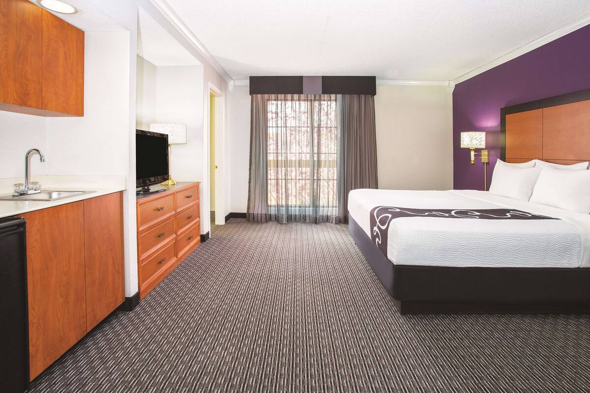 A hotel room with a bed, a desk with a sink, and a television.