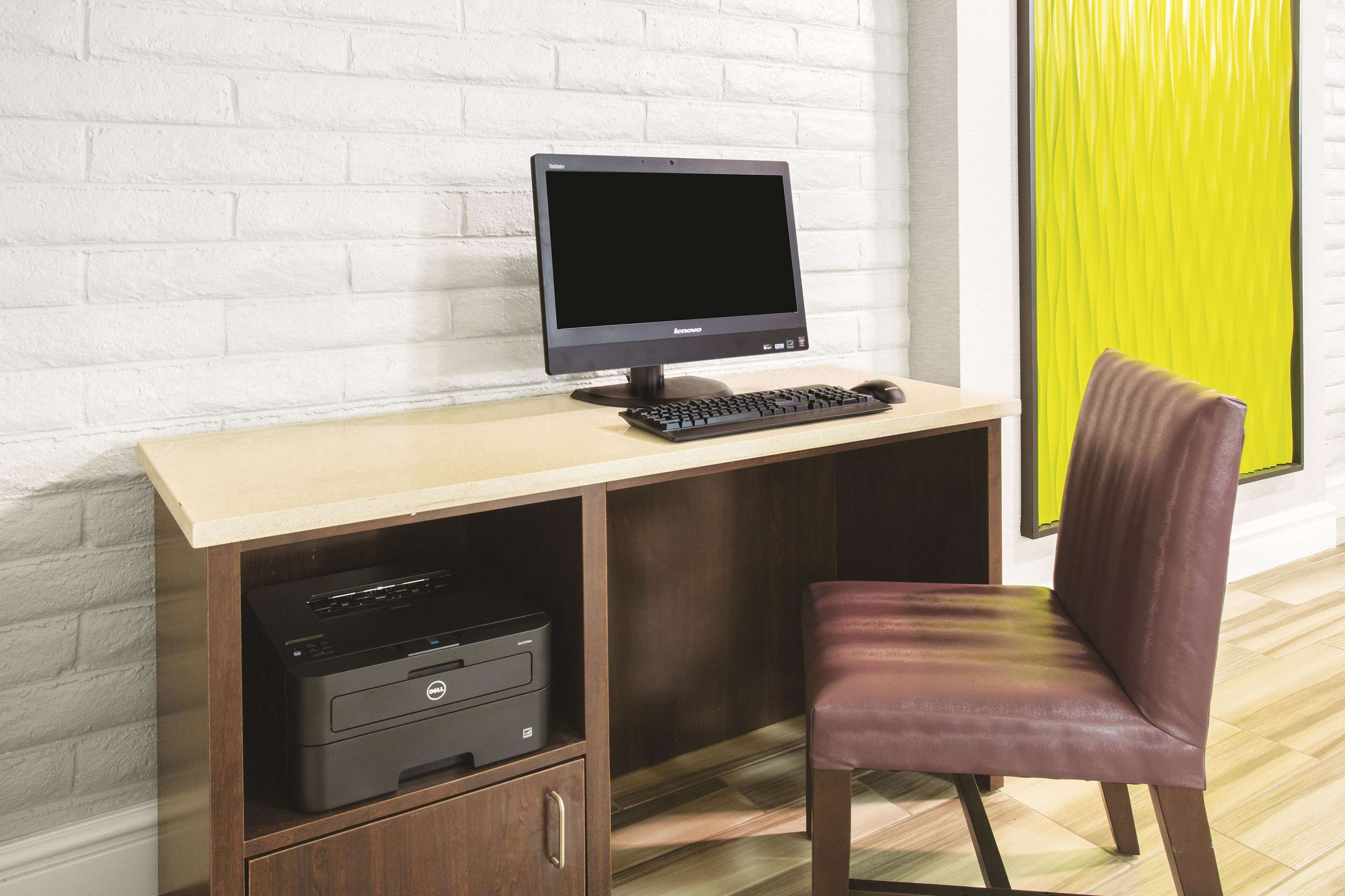 Un espace de travail comprenant un ordinateur, un clavier et une imprimante sur un bureau, une chaise et un mur en briques blanches.