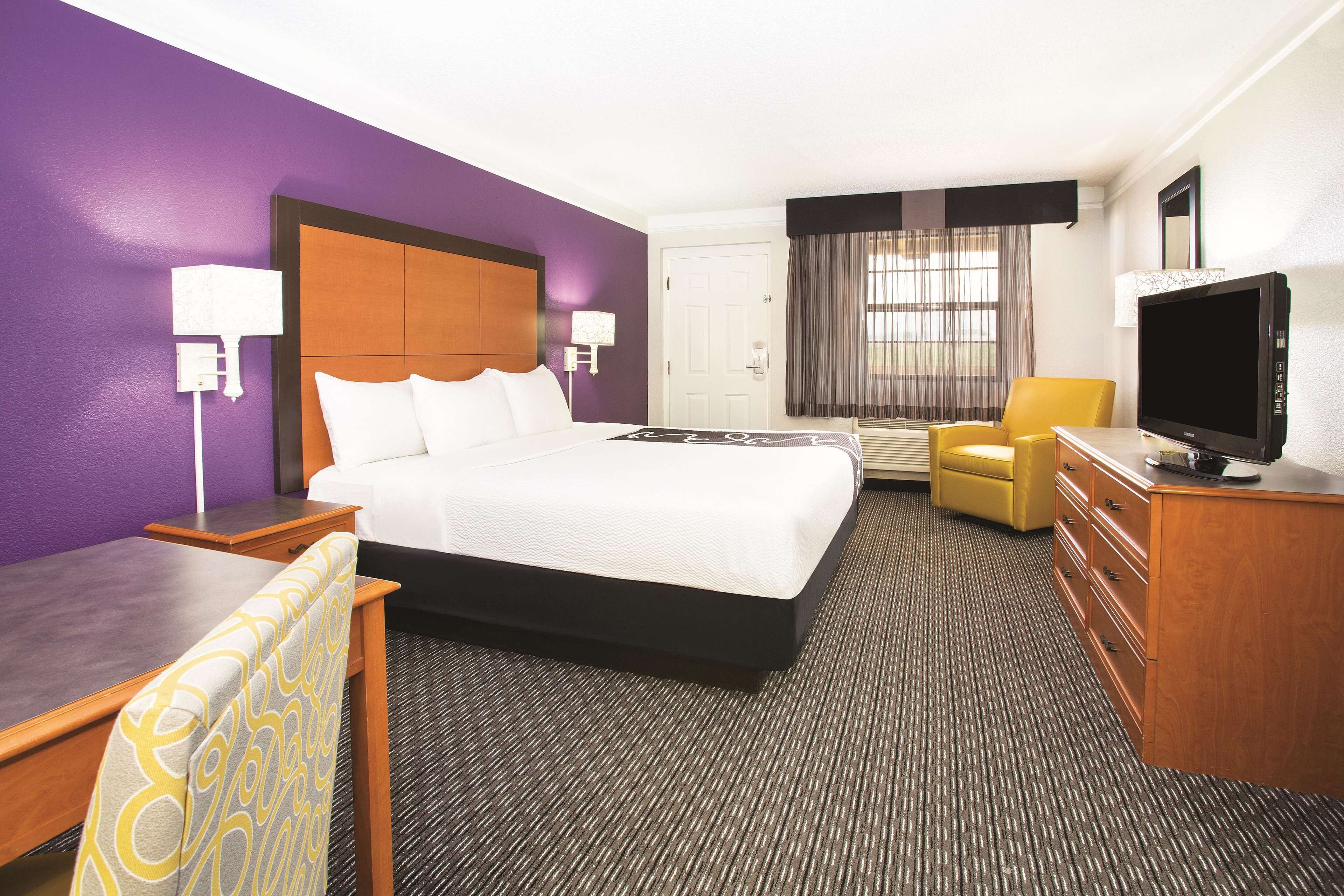A hotel room with a large bed, a desk, a chair, a television, and a dresser.