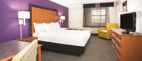 A hotel room with a large bed, a desk, a chair, a television, and a dresser.