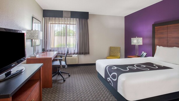A hotel room with a bed, a desk with a TV, a chair, a lamp, and a window with curtains. - La Quinta Inn by Wyndham Denver Westminster (Westminster)