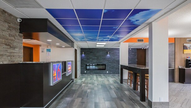 A modern lobby with a wooden reception desk, a digital screen, and a ceiling with a sky-like design.