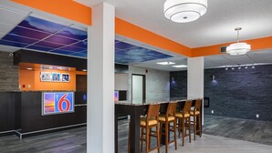 A modern lobby with a reception desk, a bar area with stools, and a stone wall.