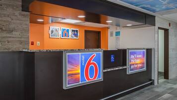 A hotel reception area with a large '6' sign, a digital display with a sunset image, and a sign stating 'We'll leave the light on for you.'
