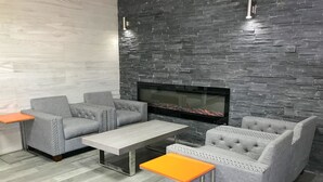 A modern living room with grey upholstered sofas, a glass coffee table, and a stone wall backdrop.
