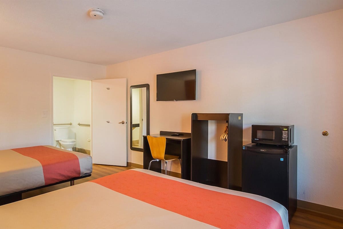 A hotel room with two beds, a desk with a chair, a television, a microwave, and a refrigerator.