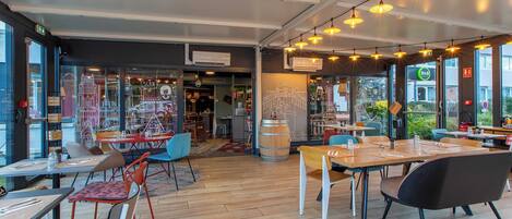 Un interior de restaurante moderno con suelo de madera, varias mesas y sillas, y lámparas colgantes.