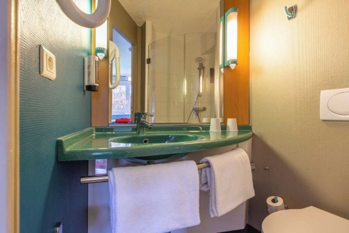 A bathroom with a green sink, a mirror, a towel rack, and a toilet.