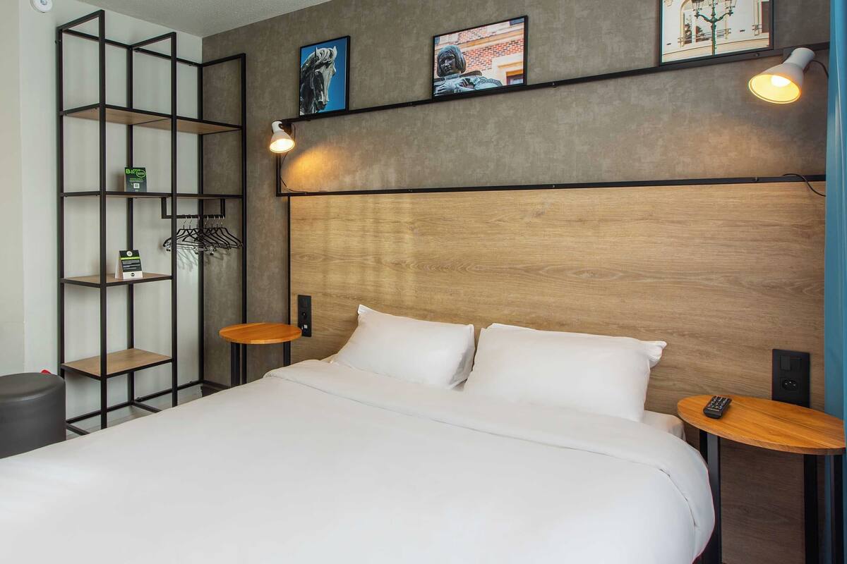 A neatly made bed with white linens, a wooden headboard, and two bedside tables with lamps.