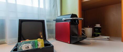 A kitchen area with a coffee machine, a box of tea bags, and a coffee maker on the counter.