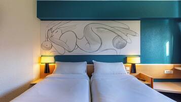 A hotel room with a large bed, two bedside tables, two lamps, and a wall art piece.