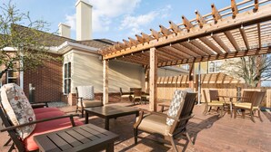 Un patio al aire libre con mobiliario de madera, una pérgola y suelo de ladrillo.