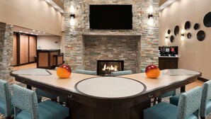 Un moderno vestíbulo de hotel con chimenea de piedra, televisor de pantalla plana y una mesa de comedor redonda con sillas.