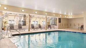 Una piscina interior con paredes de vidrio transparente, varias sillas de descanso y suelo de baldosas.