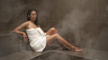 A person sitting on a bench in a steam room with tiled walls.
