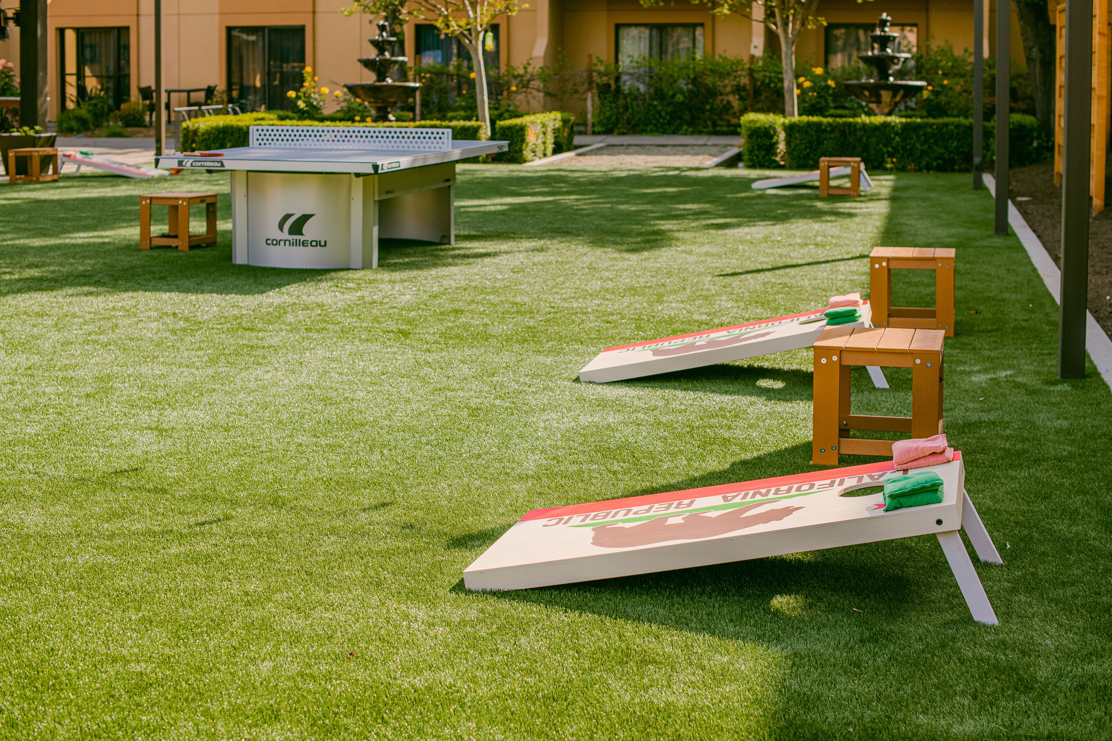 A ping pong table and chairs in a grassy outdoor area with a building in the background.