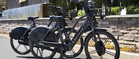 A black bicycle with a basket and a seat, parked on a paved surface.
