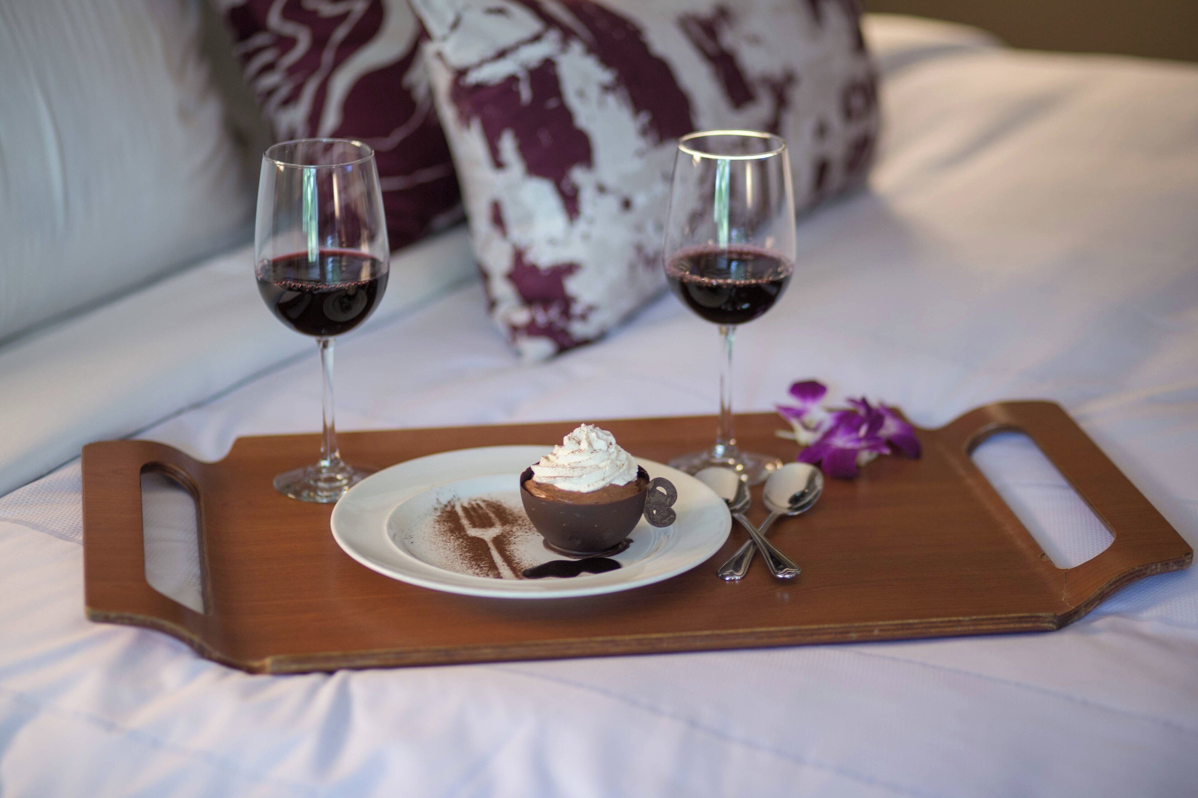 Una bandeja con un cupcake de chocolate y dos copas de vino tinto sobre una mesita.