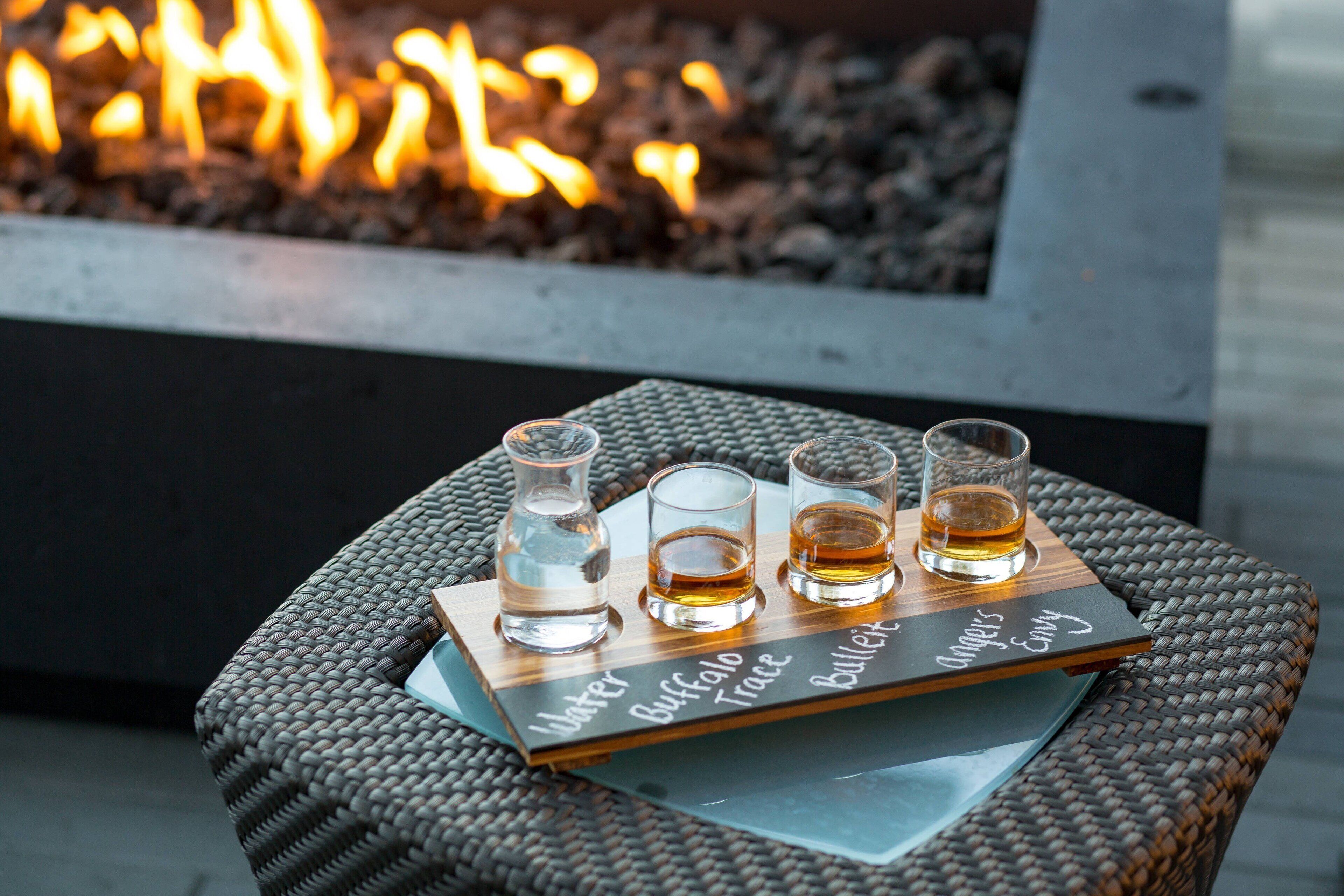 A tray with four shot glasses on a wicker table, with a fire in the background.