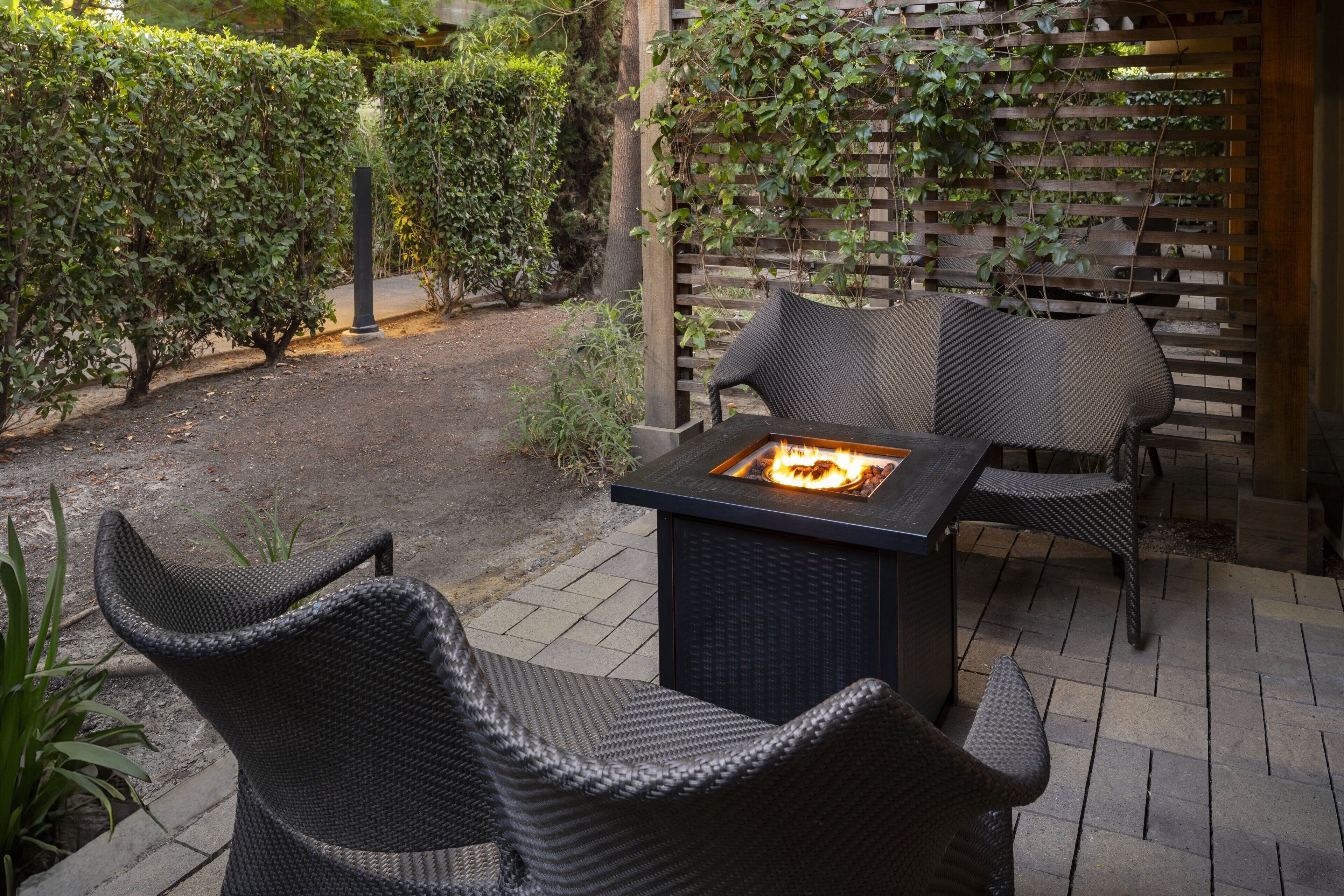 Un espacio al aire libre con asientos, una chimenea, rodeado de follaje y un muro de celosía de madera.