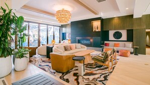 A modern living room with a large sofa, a coffee table, and a chandelier. There are potted plants and a fireplace. - Napa Valley Marriott Hotel & Spa (Napa)